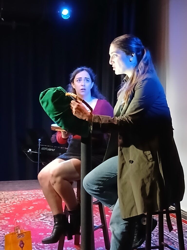 A blonde, female-presenting person stares into a bright light emanating from a green handbag, while another female-presenting person looks at her with concern.
